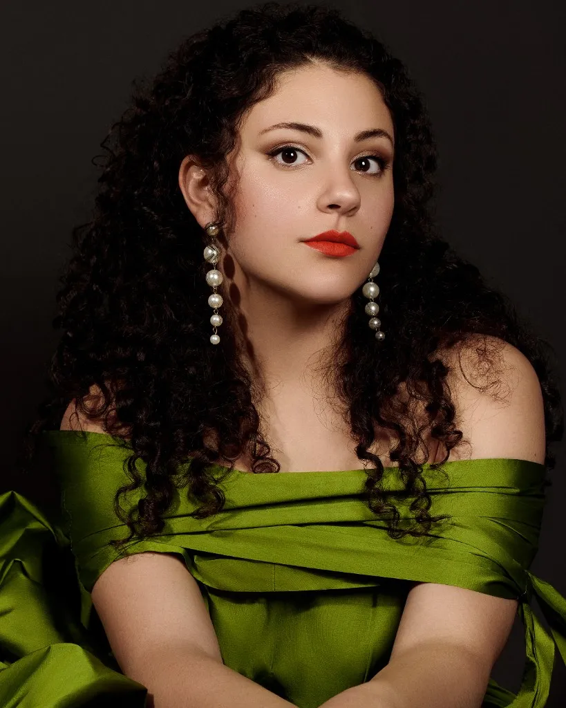 Studio portrait of Althea Troisi, soprano, in an olive-green off-the-shoulder top against a dark background.